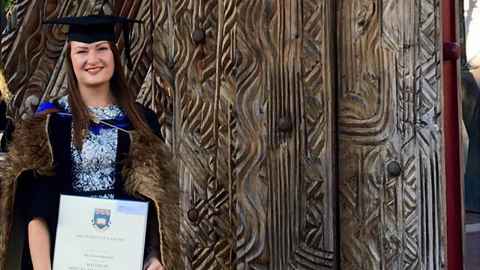 An image of Amy in her graduate gown and gap, holding her certificate